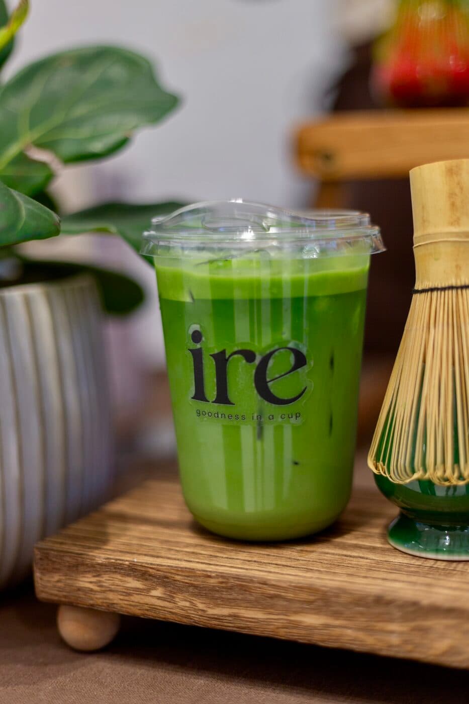 A cup of matcha beside the bamboo whisk it was made with
